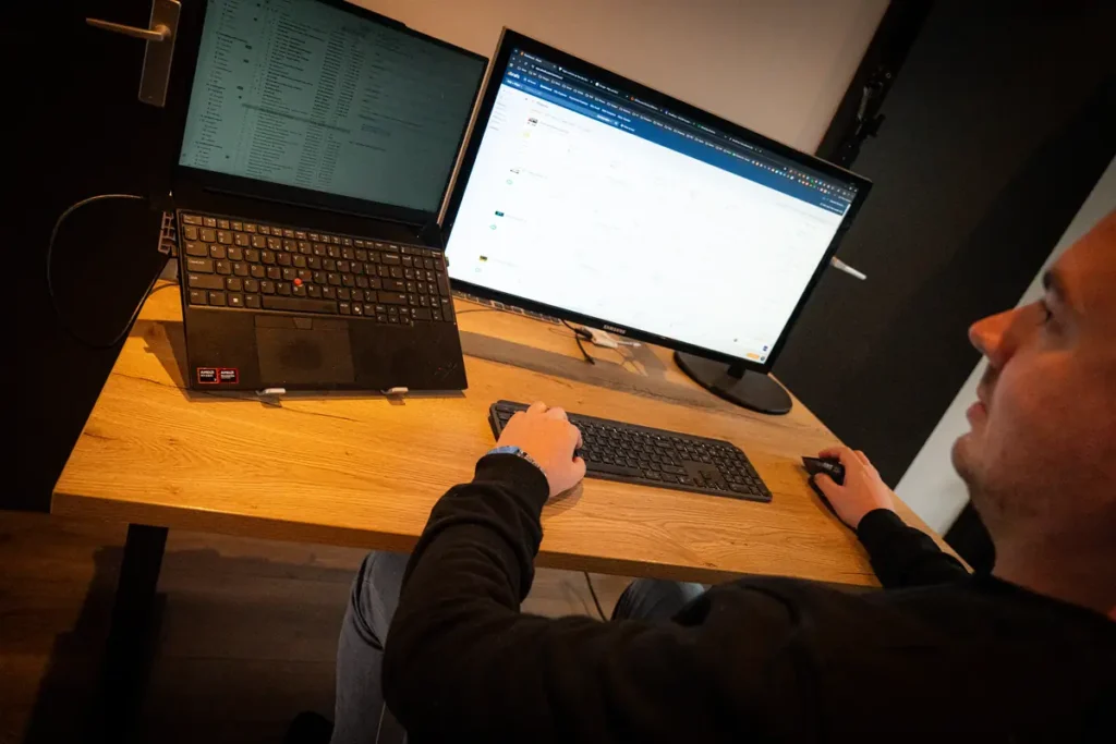 Tom aan het werk achter zijn bureau met laptop en monitor